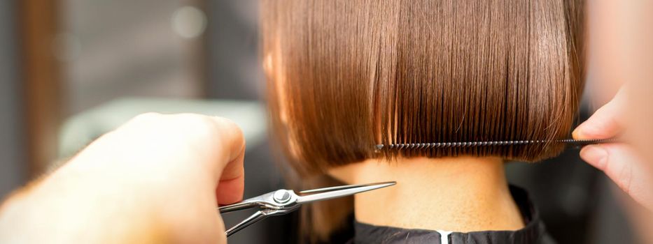 Haircut of short hair of young white woman by hands of a hairdresser in a hair salon, back view, close up