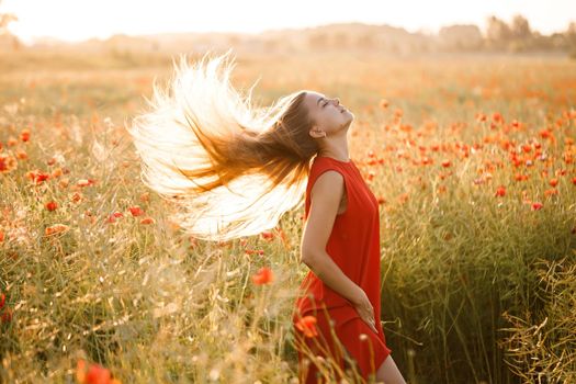 Beautiful woman in a red dress in a field of blooming poppies. Selective focus