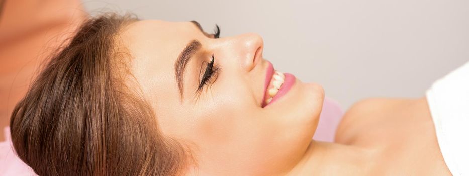 A beautiful smiling young woman is lying on a massage couch waiting for a massage in a massage room