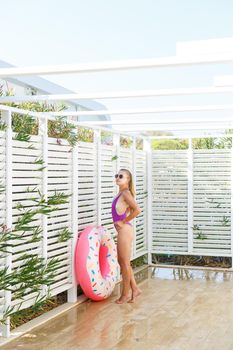 Happy young woman in stylish sunglasses and swimsuit with inflatable ring on vacation. Attractive tender girl in the sun, sunbathing and relaxing