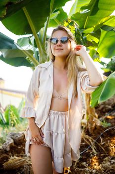 Woman near a large green leaf of a banana tree in nature in the park. Tropical plants and attractive girl walking