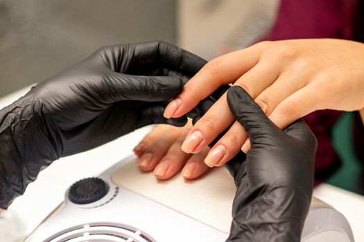 Close up professional manicure master holds the female hand of the customer and checks the manicure in a nail salon