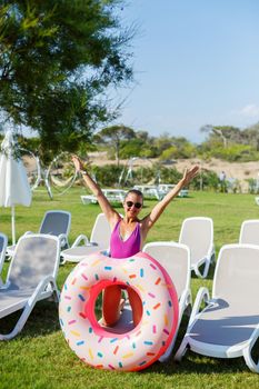 A young woman in a stylish swimsuit and sunglasses holds an inflatable donut ring in her hand. Beautiful happy girl posing and having fun in the sun. Vacation. travel