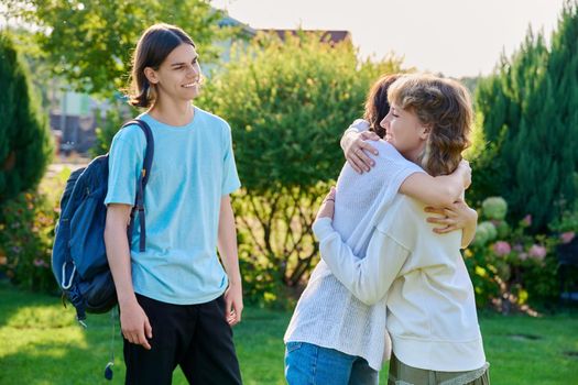 Meeting of three teenage friends, outdoor on a sunny day. Teenagers 17, 18 years old hugging, rejoicing, greeting, communication lifestyle friendship youth concept