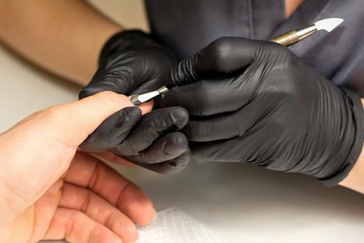 Close up professional manicurist master holding customer hand while using a cuticle pusher in a nail salon