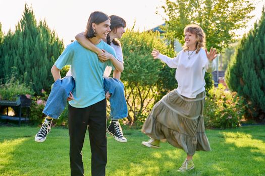 Three teenage friends having fun outdoor, sunny summer day on the lawn. Group of teenagers laughing together. Lifestyle, leisure, friendship, youth concept