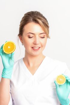 Smiling female nutritionist holding a sliced orange, looking at camera over white background, healthy diet concept