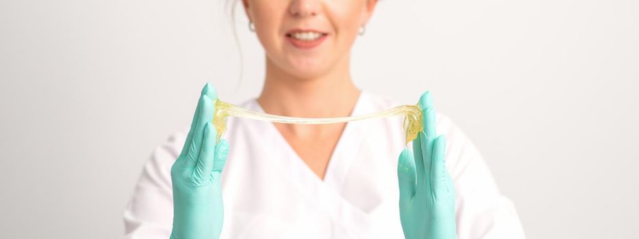 Young caucasian smiling female beautician holding wax for depilation over white background. Yellow sugar paste in hands master of depilation. Epilation concept