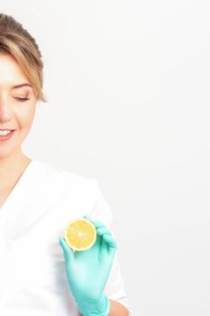 Smiling female nutritionist holding a sliced orange, looking at camera over white background, healthy diet concept