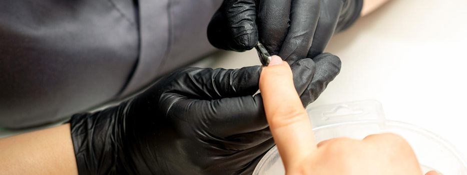 Close up professional manicurist master holding customer hand while using a cuticle pusher in a nail salon