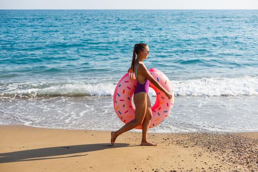 Woman on the beach walks with an inflatable ring in the sea, walks relaxing in a tropical paradise for relaxation. Young model sunbathing on summer vacation.