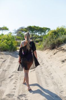 A slender tanned young woman in a swimsuit and a pareo, standing on the golden sand in the desert. Model woman resting and sunbathing on vacation. Travel concept, swimwear