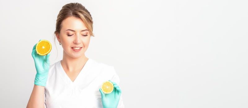 Smiling female nutritionist holding a sliced orange, looking at camera over white background, healthy diet concept