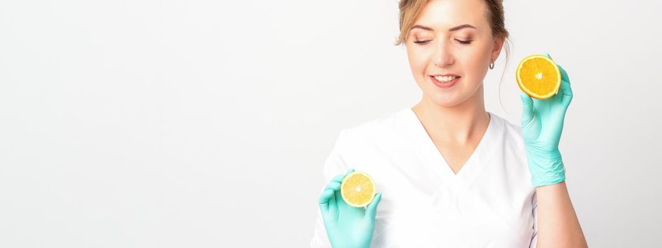 Smiling female nutritionist holding a sliced orange, looking at camera over white background, healthy diet concept