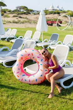 A slender young woman holds an inflatable circle in her hands, standing on the green grass. Attractive model with perfect body. Vacation concept, girl goes swimming in the sea