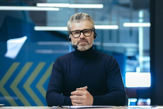 Video call, serious and mature businessman looking thoughtfully at camera, gray-haired man using headset for remote communication and online meeting.
