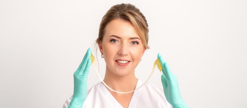 Young caucasian smiling female beautician holding wax for depilation over white background. Yellow sugar paste in hands master of depilation. Epilation concept