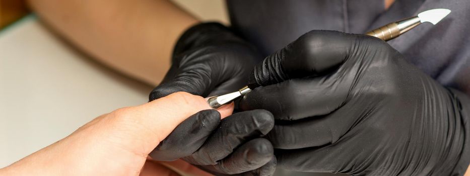 Close up professional manicurist master holding customer hand while using a cuticle pusher in a nail salon