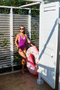 Happy young woman in stylish sunglasses and swimsuit with inflatable ring on vacation. Attractive tender girl in the sun, sunbathing and relaxing