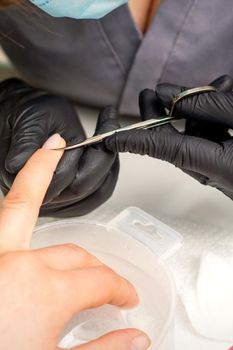 Manicure master removes cuticles from female nails with scissors wearing protective gloves in manicure salon