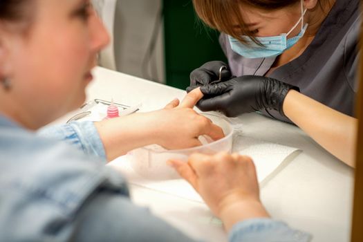 Manicure master removes cuticles from female nails with scissors wearing protective gloves in manicure salon