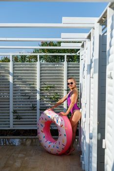 Happy young woman in stylish sunglasses and swimsuit with inflatable ring on vacation. Attractive tender girl in the sun, sunbathing and relaxing
