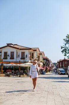 A young slender tanned woman in white shorts and a T-shirt, wearing sunglasses and a hat. Walk on a hot sunny day in the ancient city