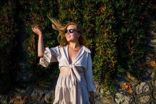 Young beautiful woman in sunglasses walks under the bright sun, she is in a beige short skirt and top