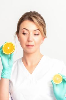 Smiling female nutritionist holding a sliced orange, looking at camera over white background, healthy diet concept