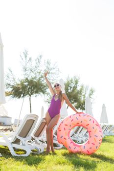 A beautiful woman holds an inflatable circle in her hands, standing on the green grass. Attractive model with perfect body. Vacation concept, the girl goes to swim in the sea.Selective focus
