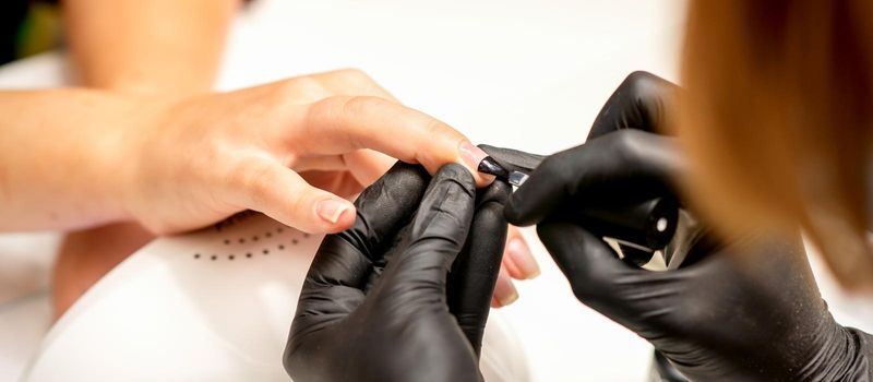 Manicure painting process. Manicure master paint the nails with transparent varnish in a nail salon, close up