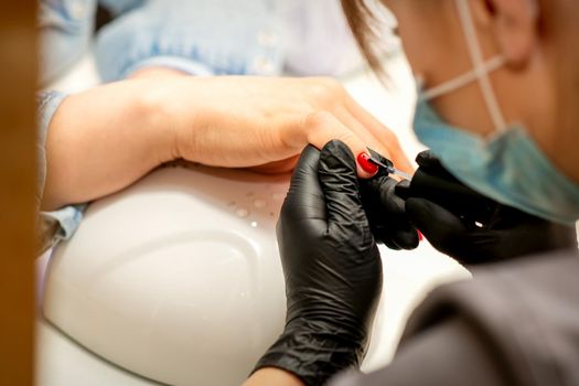 Professional manicure. A manicurist is painting the female nails of a client with red nail polish in a beauty salon, close up. Beauty industry concept