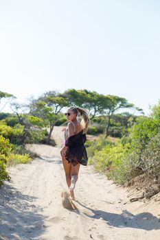A slender tanned young woman in a swimsuit and a pareo, standing on the golden sand in the desert. Model woman resting and sunbathing on vacation. Travel concept, swimwear