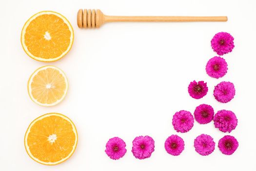 A flat lay of slices of orange fruit with red orchid petals and a wooden honey spoon lying on white background, copy space