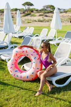 A slender young woman holds an inflatable circle in her hands, standing on the green grass. Attractive model with perfect body. Vacation concept, girl goes swimming in the sea