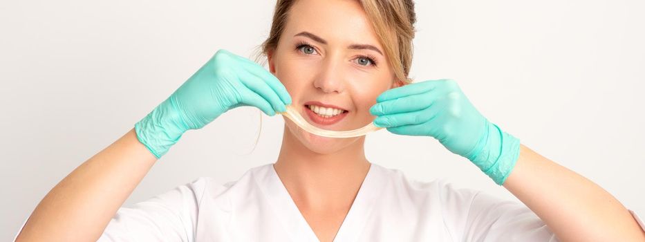 Young caucasian smiling female beautician holding wax for depilation over white background. Yellow sugar paste in hands master of depilation. Epilation concept