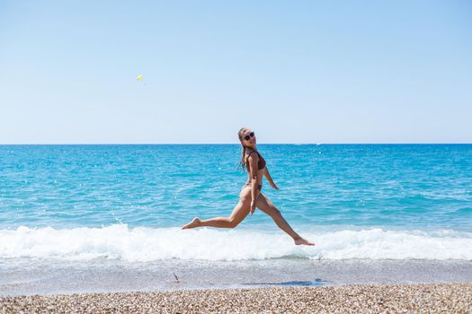A slender beautiful young woman in a swimsuit walks along the beach by the sea. Summer vacation concept. Selective focus