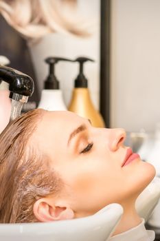 Young caucasian woman with closed eyes getting washing hair by a professional hairdresser in a beauty hair salon