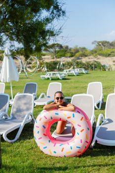 A young woman in a stylish swimsuit and sunglasses holds an inflatable donut ring in her hand. Beautiful happy girl posing and having fun in the sun. Vacation. travel