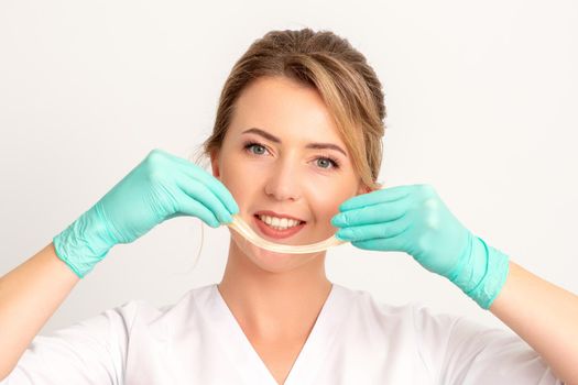 Young caucasian smiling female beautician holding wax for depilation over white background. Yellow sugar paste in hands master of depilation. Epilation concept