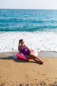 Vacation at the sea. Beautiful slender woman in a swimsuit with an inflatable ring on the beach. Girl resting in the summer on the turkish coast