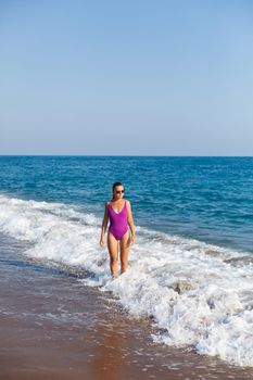 Beautiful woman with a toned body in a bright swimsuit walks along the sandy beach. Summer vacation at the sea. Mediterranean Turkish Sea. Selective focus
