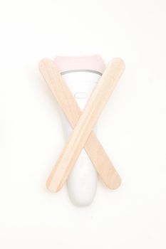 Waxing, depilation concept. Flat lay of the white epilator with wooden sticks lying on white background