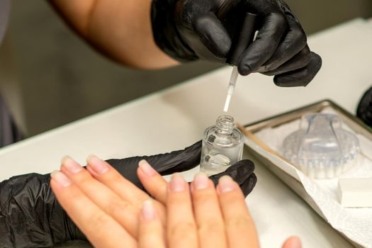 Manicure painting process. Manicure master paint the nails with transparent varnish in a nail salon, close up