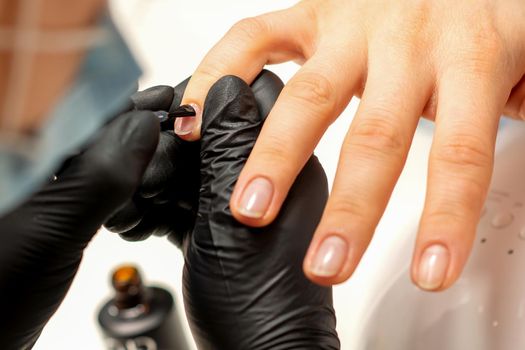 Manicure painting process. Manicure master paint the nails with transparent varnish in a nail salon, close up