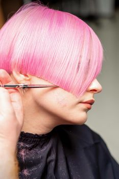 Hand of a hairdresser cutting short pink with scissor hair in a hairdressing salon, close up, side view