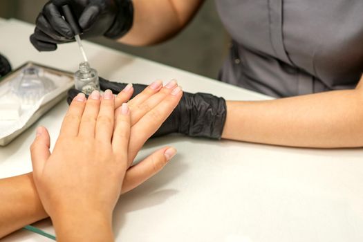 Manicure painting process. Manicure master paint the nails with transparent varnish in a nail salon, close up