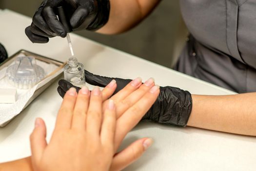 Manicure painting process. Manicure master paint the nails with transparent varnish in a nail salon, close up