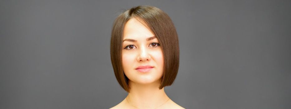 Beautiful young caucasian brunette woman with short hairstyle smiling and looking at camera against dark gray background with copy space