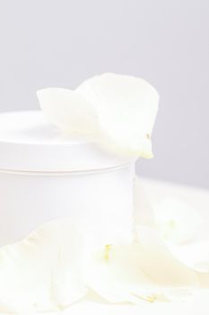 White jar with cream among delicate white rose flowers petals on a light background. Natural organic cosmetics concept, close up, mock-up